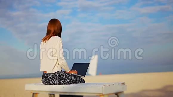 在阳光明媚的海滩上用笔记本电脑工作的女孩视频的预览图