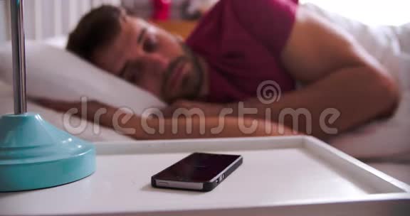 男人在床上醒来检查手机上的信息视频的预览图