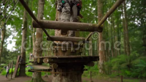 一个穿着安全装备的小男孩在森林探险公园的树梢上爬上了一条路线他是视频的预览图