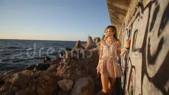 日落时分在海边的涂鸦墙上散步的女孩视频的预览图