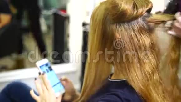 发型师的金发女孩带着智能手机视频的预览图
