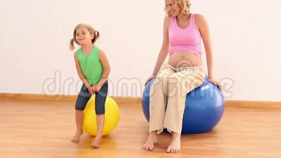 金发孕妇和她的小女孩坐在健身球上视频的预览图