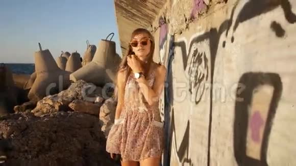 日落时分在海边的涂鸦墙上散步的女孩视频的预览图