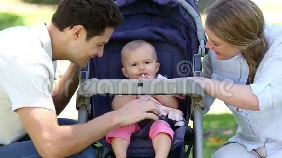 快乐的父母在公园的婴儿车里照顾女婴视频的预览图