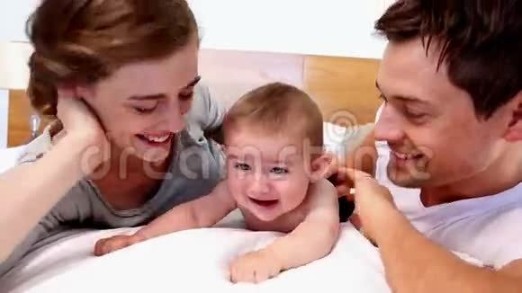 快乐的父母和他们可爱的小儿子躺在床上视频的预览图
