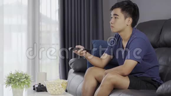 年轻人拿着遥控器坐在沙发上看电视视频的预览图