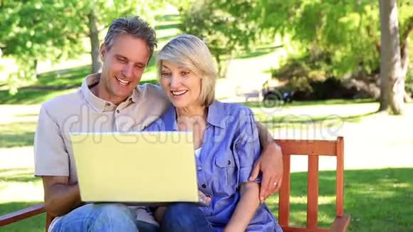 情侣坐在公园长椅上用笔记本电脑视频的预览图