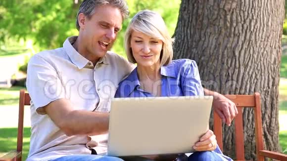 情侣坐在公园长椅上用笔记本电脑视频的预览图