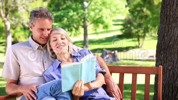 坐在公园长椅上看书的一对恩爱的夫妇视频的预览图