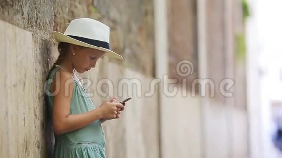 可爱的小女孩与智能手机温暖的一天户外欧洲城市视频的预览图