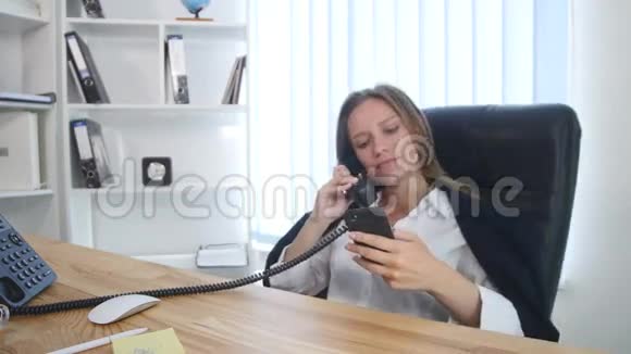 年轻漂亮的女商人在办公室里用电话和智能手机聊天微笑着视频的预览图