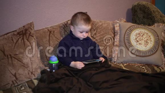 小男孩坐在沙发上看着智能手机上的卡通视频的预览图