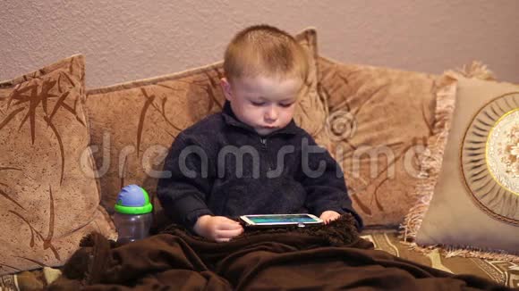 小男孩坐在沙发上看着智能手机上的卡通视频的预览图