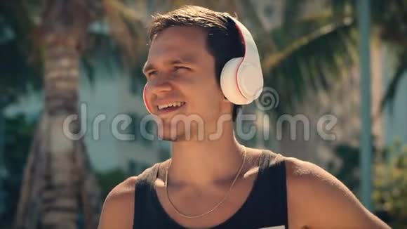 英俊的年轻人用无线耳机听他的智能手机里的音乐在海滩上跳舞视频的预览图