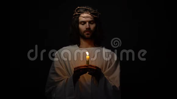 耶稣基督戴着荆棘的冠冕举着蜡烛祈求上帝保佑希望视频的预览图