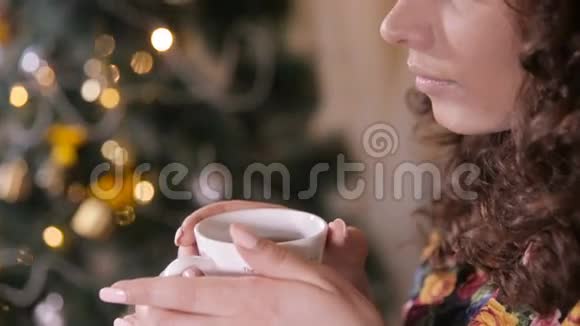 美丽的女孩在装饰圣诞树附近喝茶坐在舒适舒适的椅子上视频的预览图