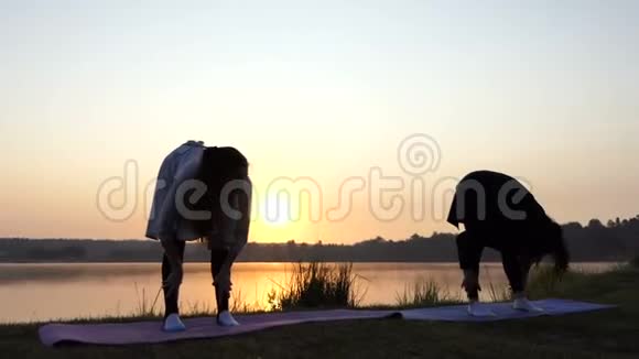 日落时两位年轻女子在风景如画的湖岸做瑜伽视频的预览图