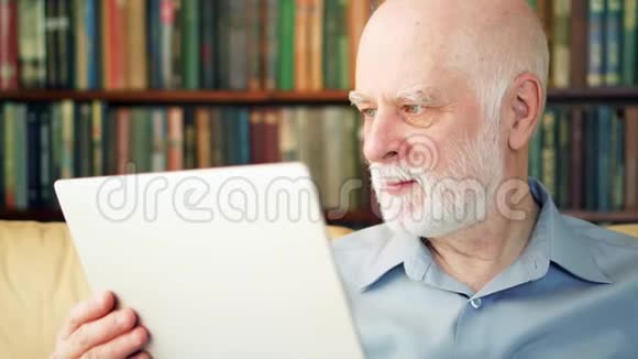 英俊的老人在家里用笔记本电脑工作退休后的远程自由职业工作视频的预览图
