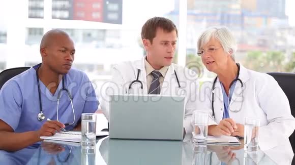 成熟的医生和她的团队坐在一起看笔记本电脑视频的预览图