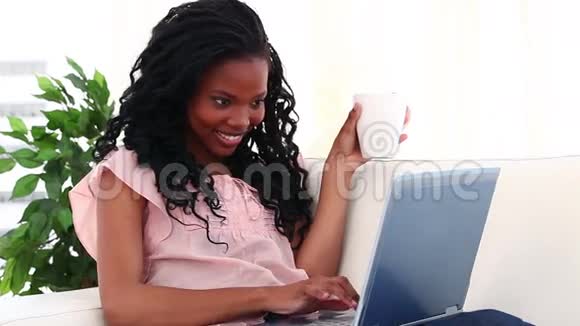 微笑的黑发女人在她的笔记本电脑前喝咖啡视频的预览图