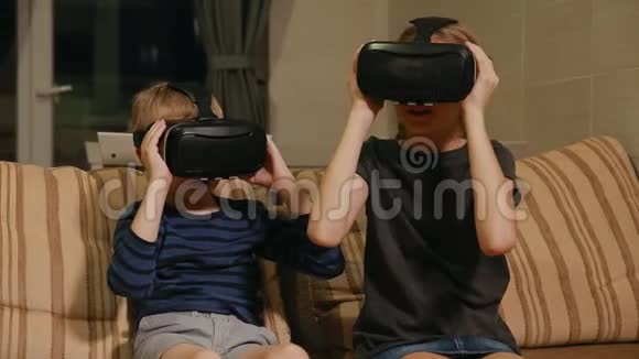 哥哥和姐姐在家坐在沙发上玩游戏用虚拟现实眼镜幸福家庭视频的预览图