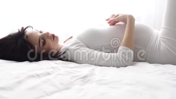 怀孕美丽的女人躺在床上抚摸婴儿的腹部视频的预览图