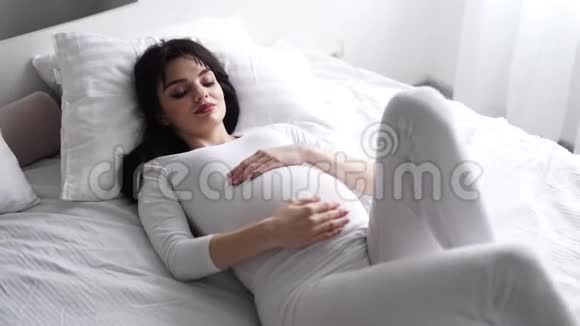 怀孕美丽的女人躺在床上抚摸婴儿的腹部视频的预览图