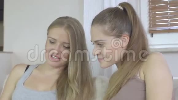 两个女孩坐在沙发上用平板电脑和微笑的录像视频的预览图