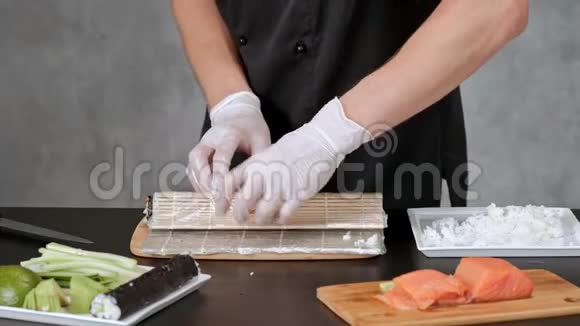 年轻的男性寿司厨师准备日本寿司卷的米饭鲑鱼鳄梨和诺里餐厅厨房双手特写视频的预览图