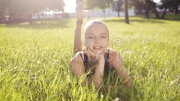 微笑的女孩躺在绿草上微笑草地上的年轻体操运动员视频的预览图