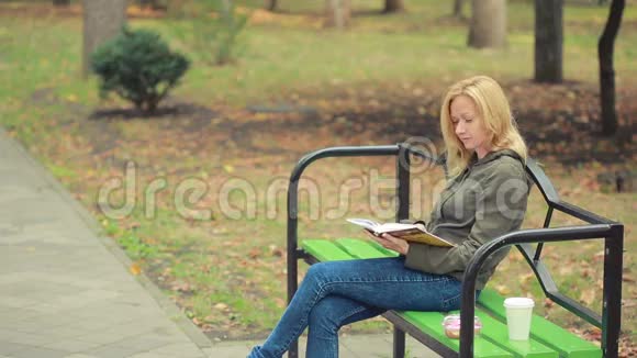 金碧辉煌的女子读书书在秋天的公园里喝热咖啡或茶视频的预览图
