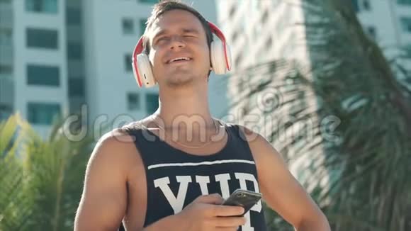 英俊的年轻人用无线耳机听他的智能手机里的音乐在海滩上跳舞视频的预览图