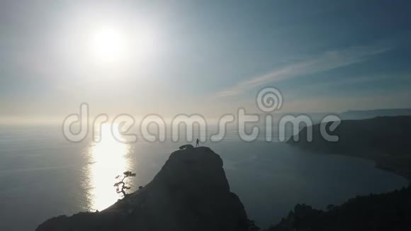 一位年轻女子站在一座面向大海的山顶上的空中轮廓在美丽的山顶上的女士视频的预览图