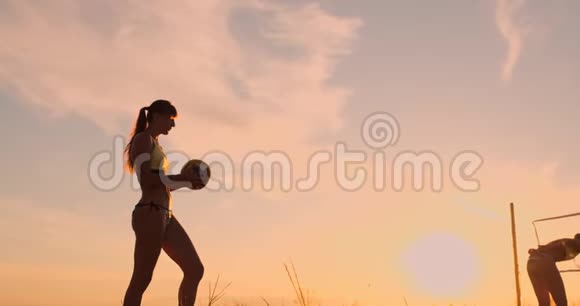 在一个美丽的夏日傍晚运动女孩在沙滩排球比赛中跳到空中在网上击球视频的预览图