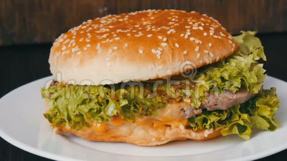 大的三层汉堡白色盘子里有生菜叶汉堡在时尚的木制背景上快餐视频的预览图