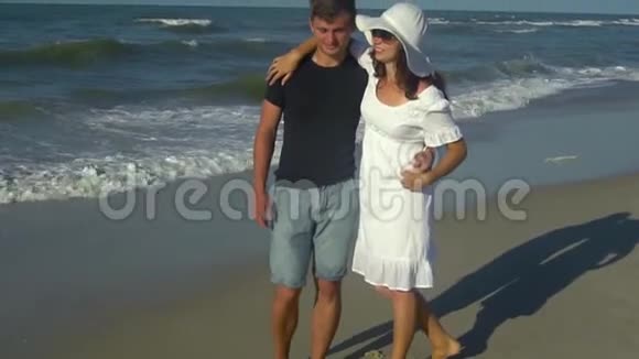 年轻漂亮的夫妇走在海边男孩和女孩他们很开心阳光灿烂慢动作他们视频的预览图