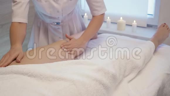 年轻女子在美容院做脚部按摩玛瑟用蜡烛揉捏一个年轻漂亮女孩的脚和腿视频的预览图