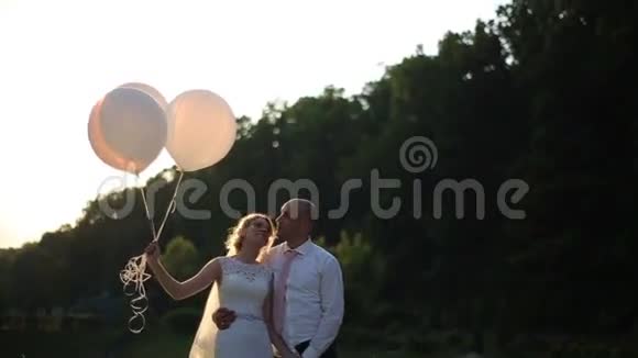 结婚那天的浪漫情侣新娘和新郎带着气球在夕阳的田野里视频的预览图