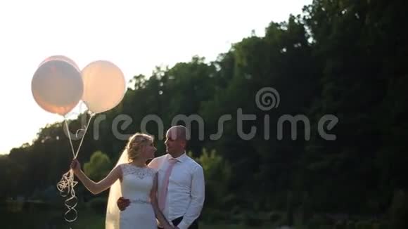 结婚那天的浪漫情侣新娘和新郎带着气球在夕阳的田野里视频的预览图