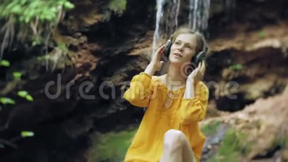 年轻时尚的美女靠近瀑布听音乐的大监控耳机视频的预览图