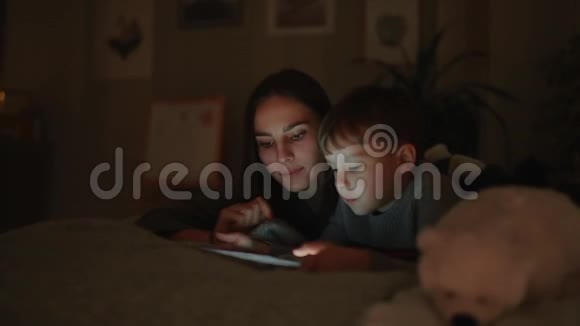 幸福的一家人母子躺在床上在他家的卧室里玩游戏屏幕上放着平板电脑视频的预览图