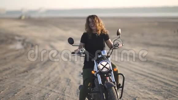 美丽的年轻女子骑着一辆古老的咖啡馆赛车摩托车在沙漠日落或日出女自行车手视频的预览图