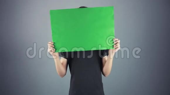 好奇的年轻人穿着黑色衬衫拿着绿色的钥匙片海报灰色的背景视频的预览图