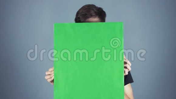 好奇的年轻人穿着黑色衬衫拿着绿色的钥匙片海报灰色的背景视频的预览图