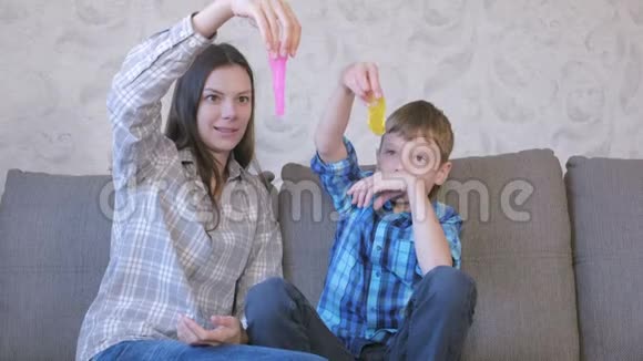 快乐的妈妈和儿子坐在沙发上玩黏液伸展的黏液视频的预览图