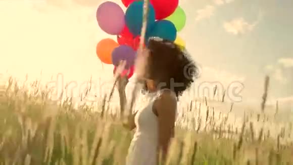日落时分年轻女孩带着彩色气球穿过麦田视频的预览图