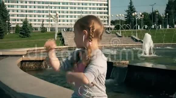 美丽的女孩在喷泉附近用手机耳机听音乐视频的预览图