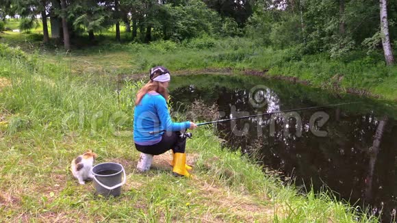 金发孕妇与可爱的猫在池塘岸边钓鱼视频的预览图