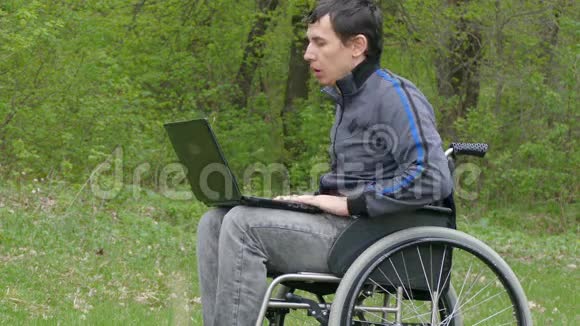 残疾人厌倦了休息问题轮椅上的笔记本电脑在自然绿色背景下工作视频的预览图