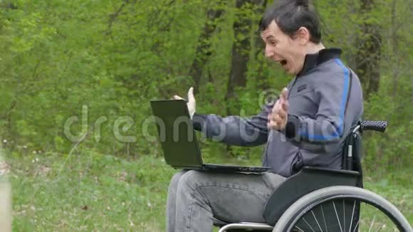 自然绿色背景下带笔记本电脑的人残疾人惊喜胜利轮椅视频的预览图